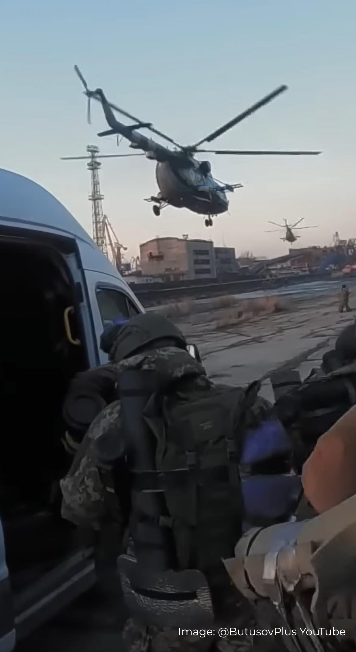 Ukrainian soldier in military gear with s Savotta Kahakka backpack in front of a van, there is a helicopter in the air, urban scenery