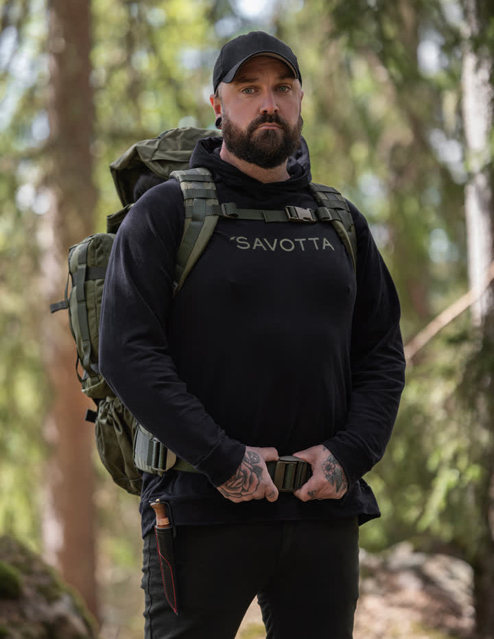 Man with a backpack and 'Savotta' hoodie standing in a forest