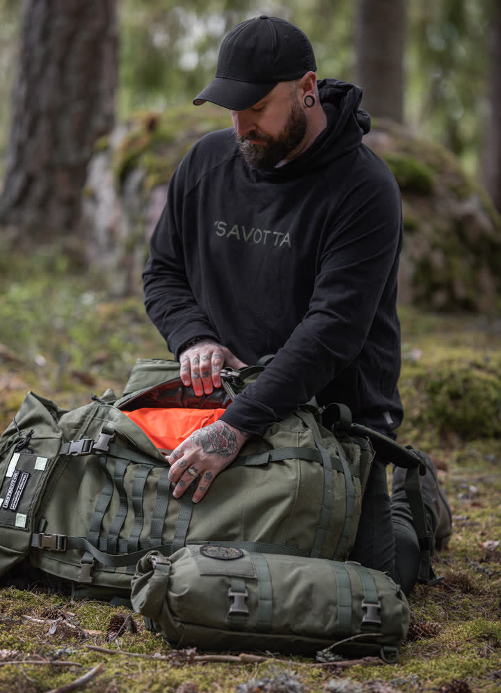 Man in black Savotta hoodie sitting with green Kantamus 60L backpack in the forest