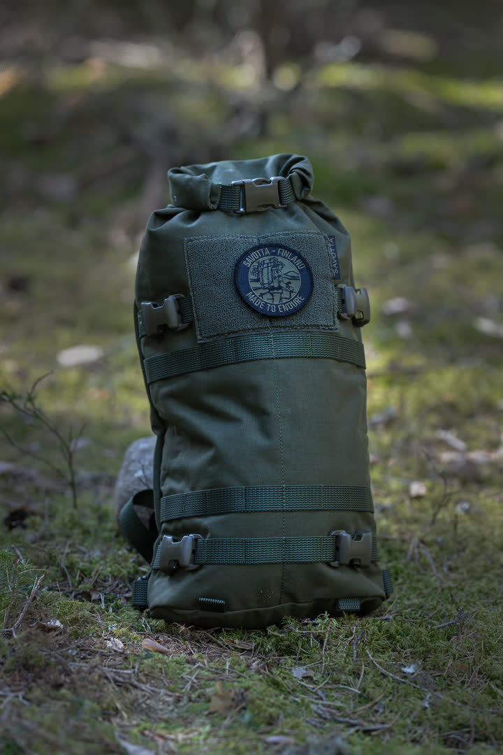 Green Savotta Hatka 12L backpack with a patch on a grassy background