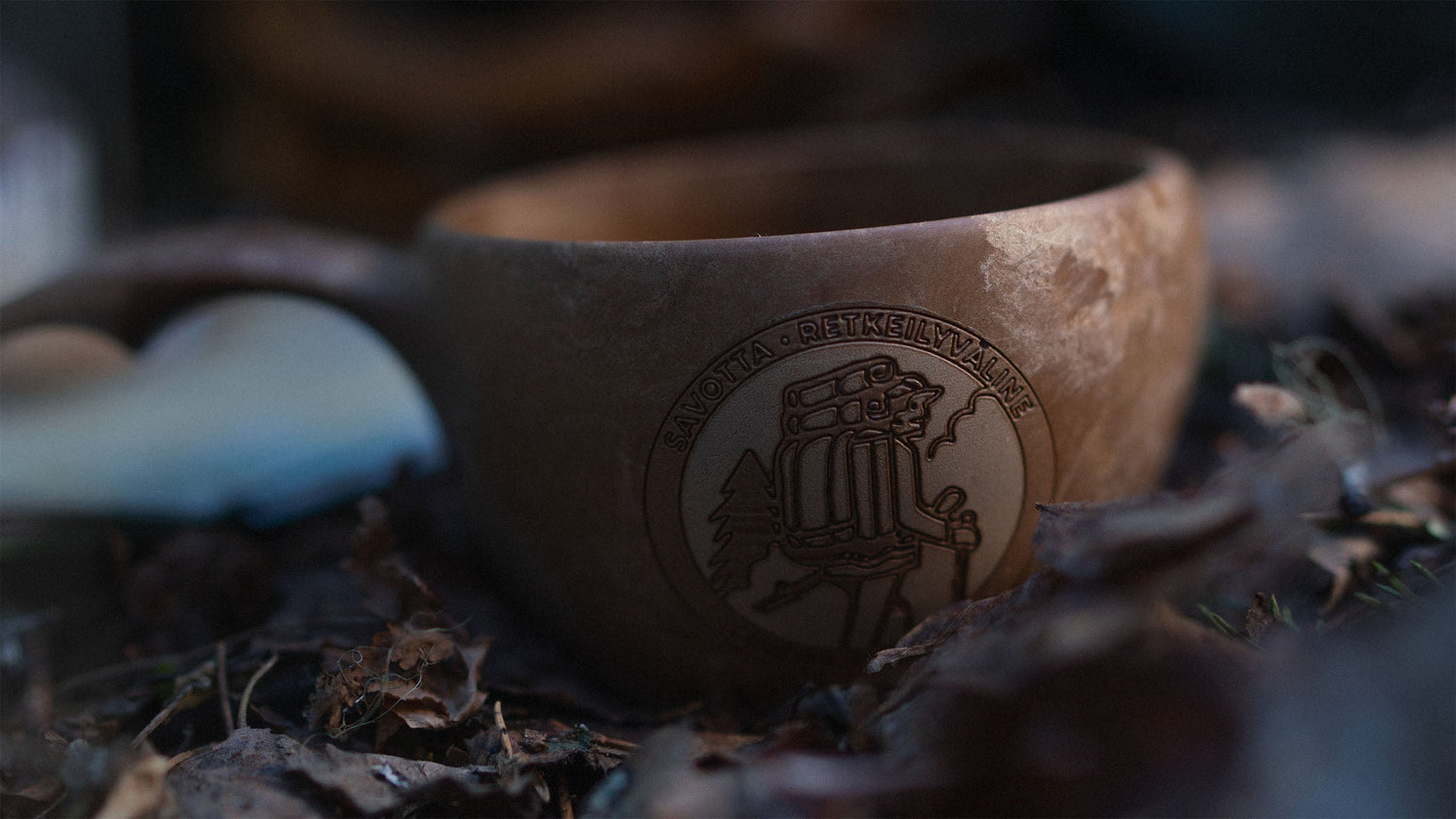 Brown Savotta x Kupilka cup with engraved Savotta logo on a natural background