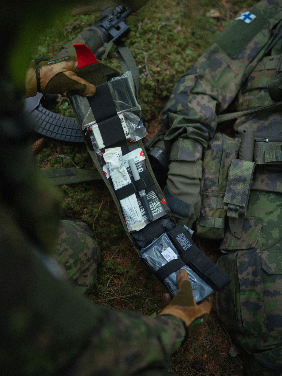 Opened-up Savotta S-IFAK insert held by soldier's hands against a mossy ground.
