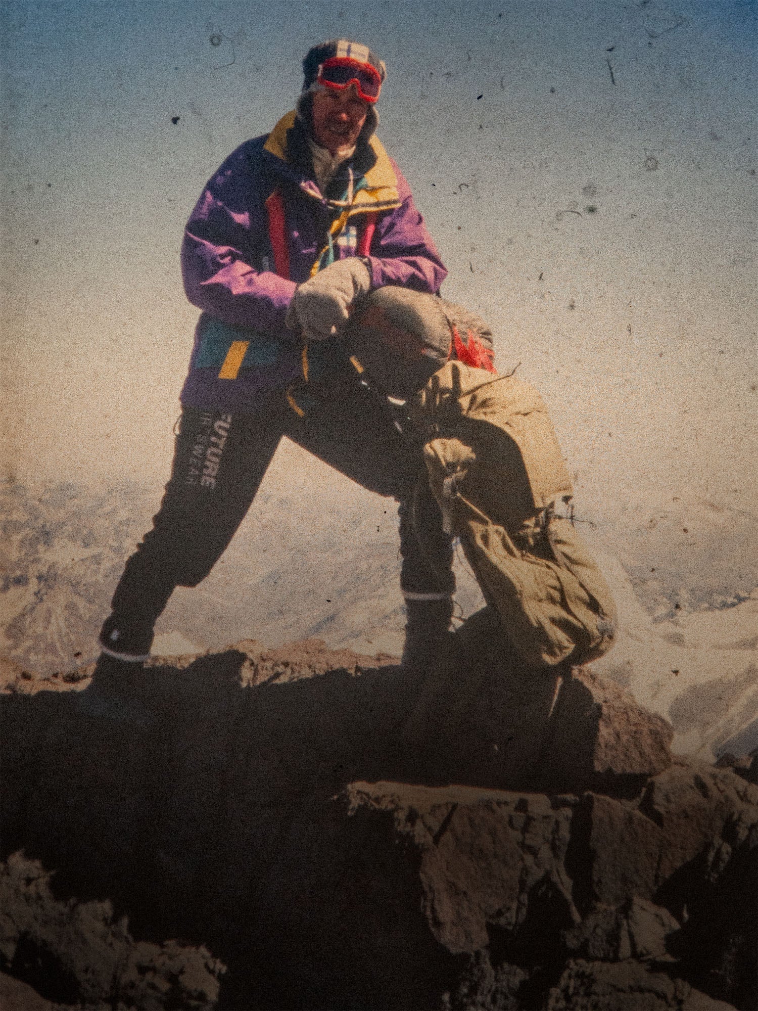 Person in colorful jacket and helmet on a mountain, leaning against an old Savotta backpack