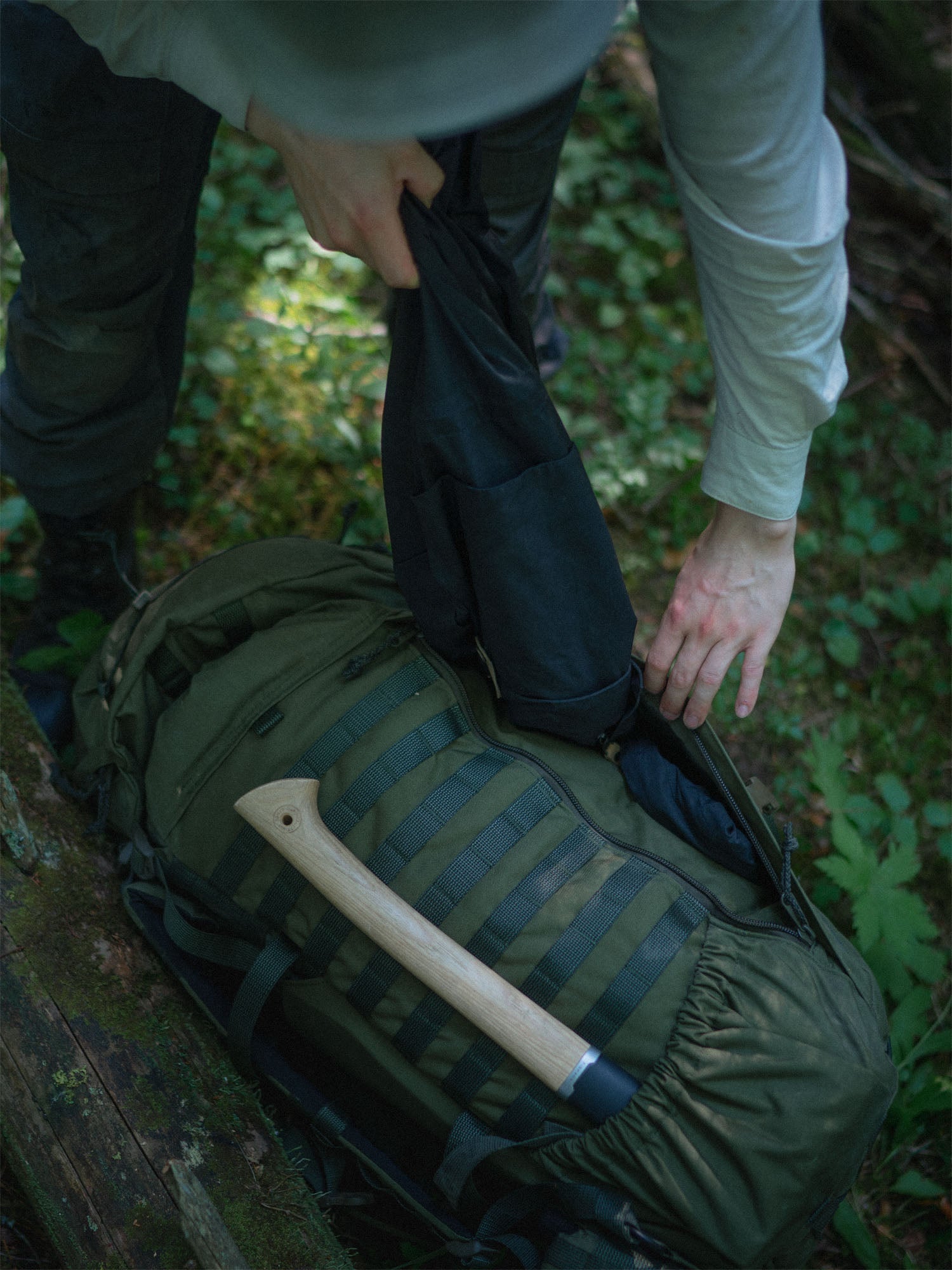 Person taking a jacket out of the front zipper pouch of a flat compartment of the Savotta Kantamus 60L on a forest floor