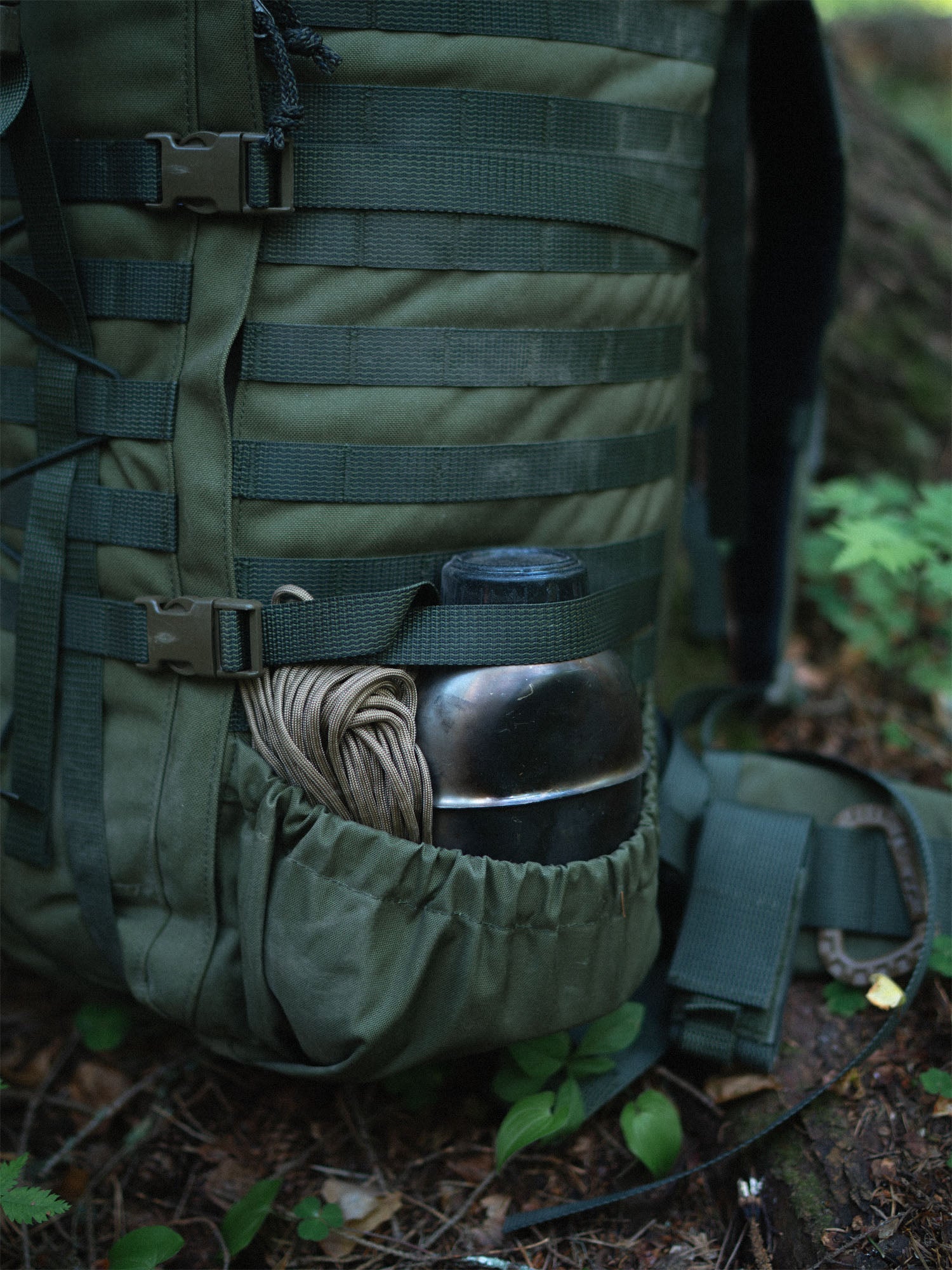 Side pouch of a Savotta Kantamus 60L containing a bottle and coiled rope in a forest setting.