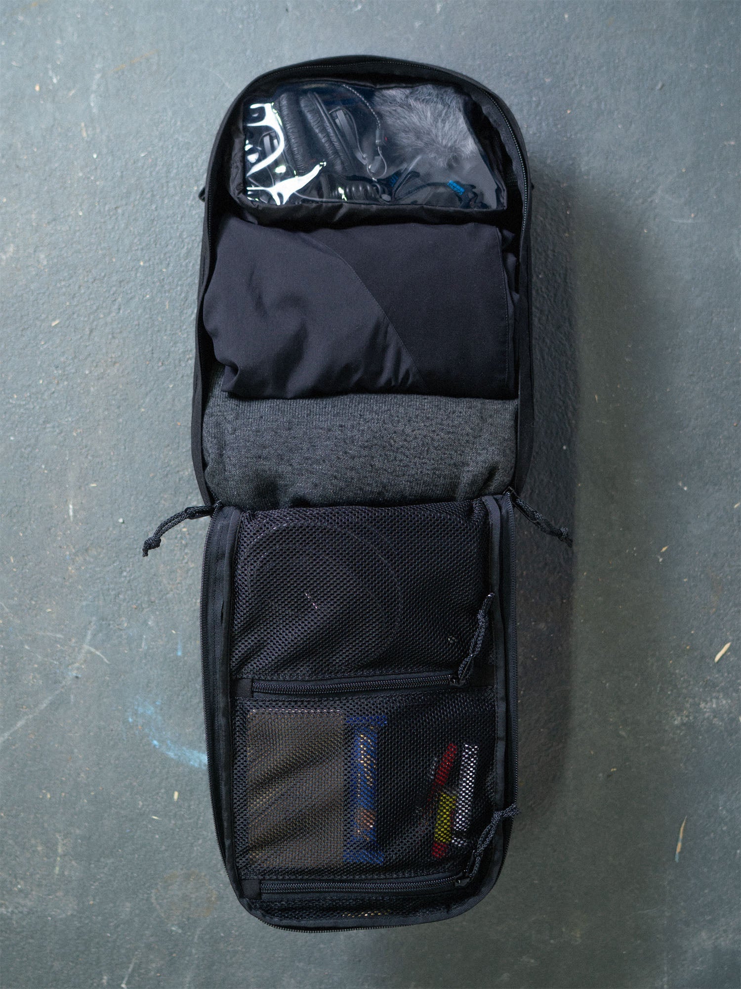 A filled black Savotta Niukka 20L backpack fully opened up on a grey surface