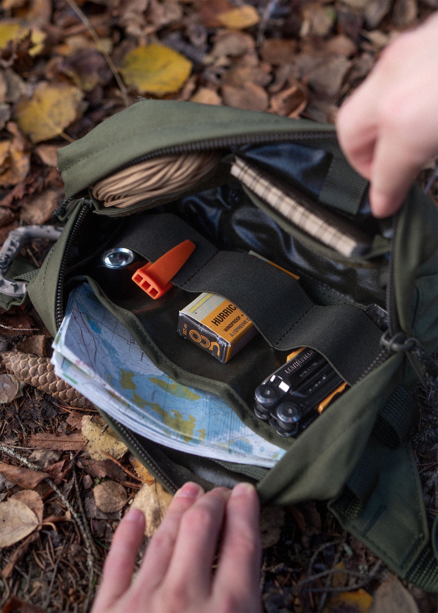 Savotta Suur-Kukkaro hip pack being opened on a forest ground, there are different tools inside the pack