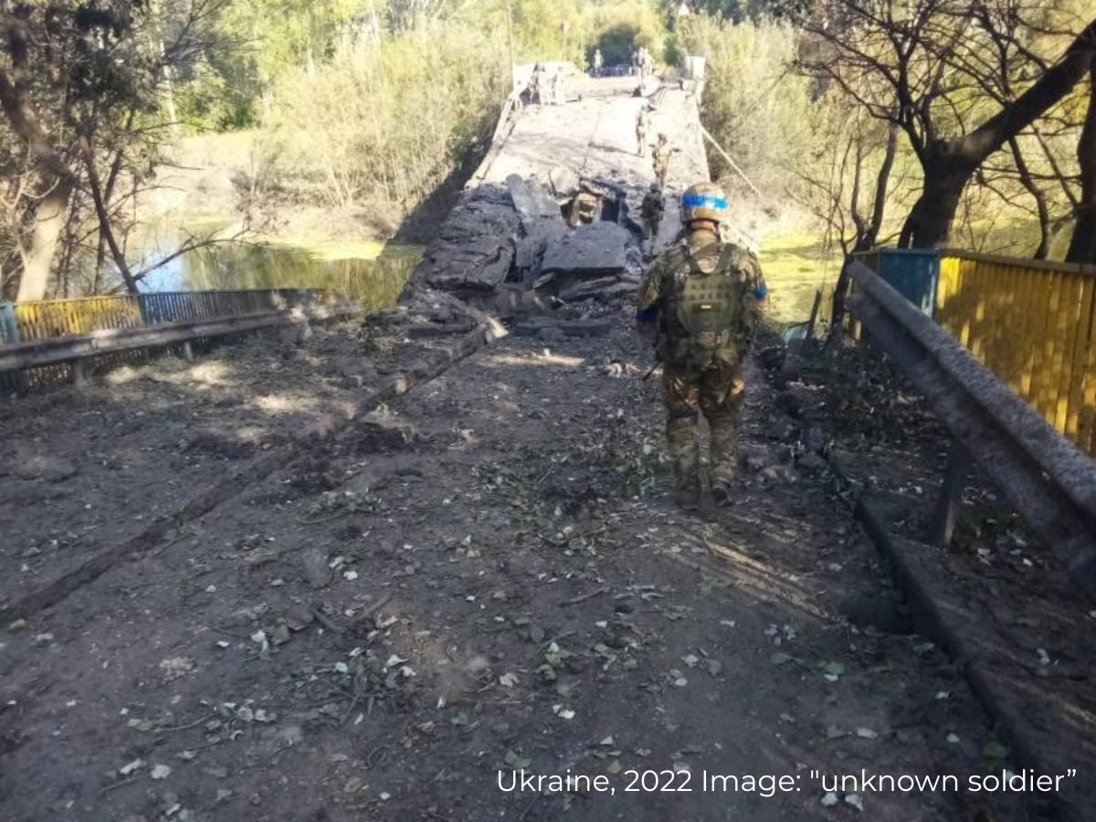 Ukrainian soldier in military uniform walking on a damaged bridge with trees and water in the background