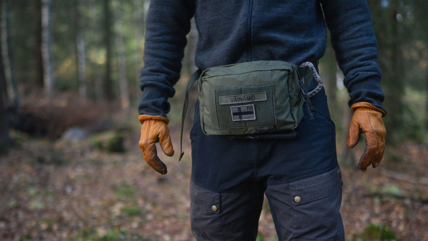 Person in a forest wearing a Savotta Suur-kukkaro hip pack and brown gloves.