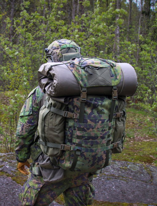 Person in camouflage military uniform with a Savotta Kantamus 40L backpack and side pouches attached walking through a forest.