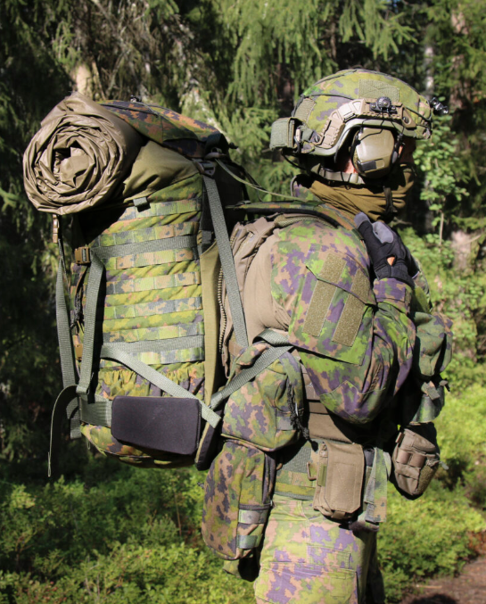Person in camouflage gear with a Savotta Kantamus 60L in a sunny forest setting