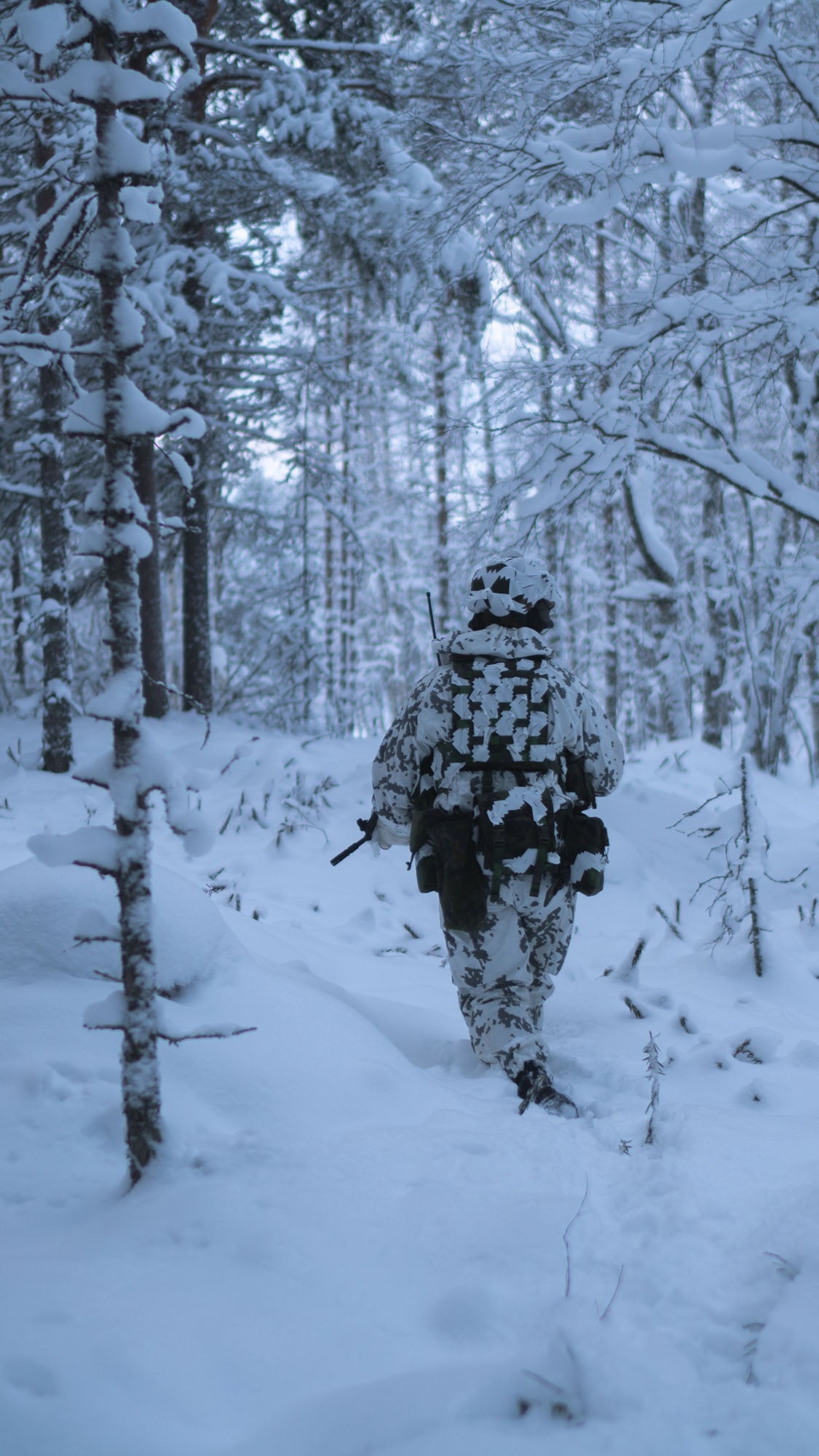 Person in winter camouflage gear walking through a snowy forest