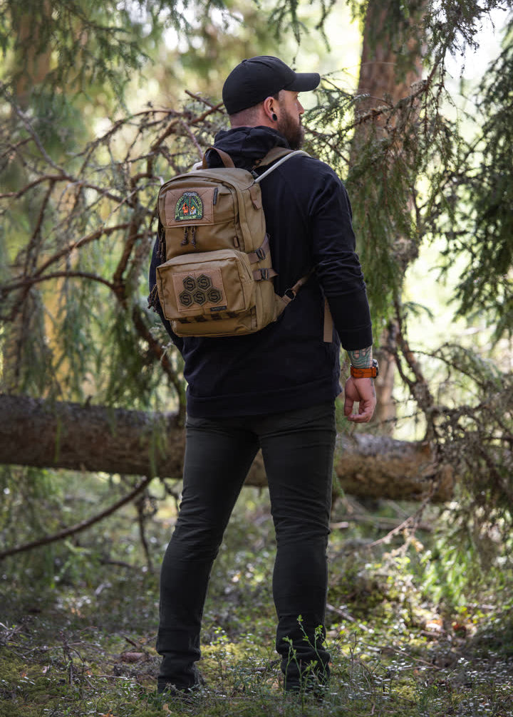 Person wearing a brown Savotta Niukka 20L backpack with a Suur-Kukkaro hip pack attached ans a patch in a forest setting