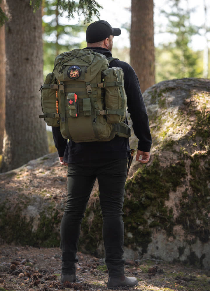 Person wearing a green Kantamus 40L backpack with 6L side pouches in a forest setting
