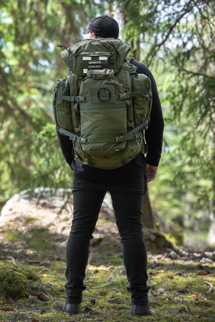 Person wearing a green Savotta Kantamus 60L backpack with a Hatka 12L attached, in a forest setting