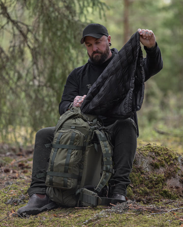 Man in a forest setting with a green Kantamus 40L backpack and black jacket.