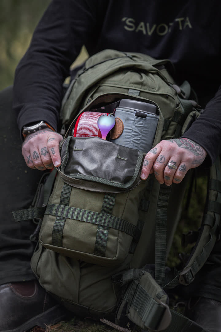 Person opening a green side pouch on a Kantamus backpack with items inside, wearing a black hoodie with 'Savotta' branding.