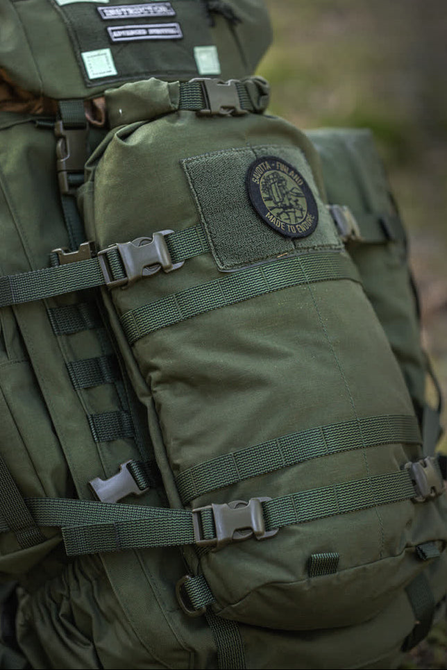 Green Savotta backpack with patches on a blurred natural background