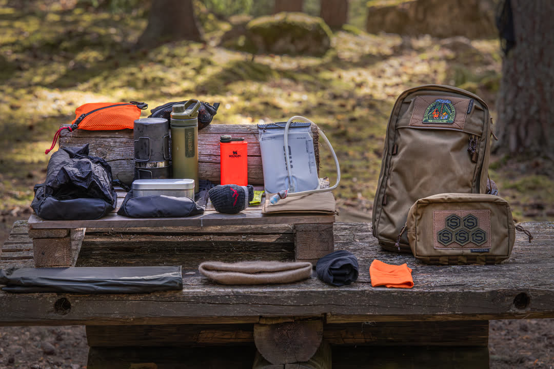 Collection of outdoor gear including a backpack, water bottles, and pouches on a wooden table with a natural background.