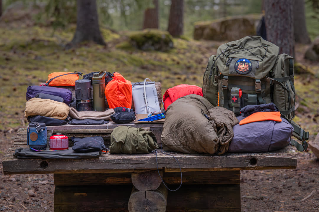 Assorted outdoor gear on a wooden table in a forest setting