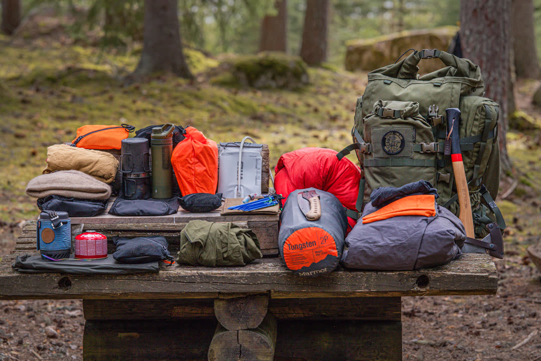 Collection of outdoor gear on a wooden table in a forest setting