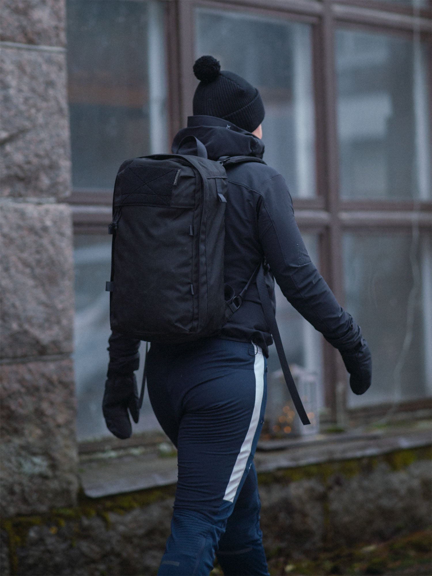 Sporty person wearing a black Savotta Niukka 20L backpack and black outdoor clothing walking outdoors.