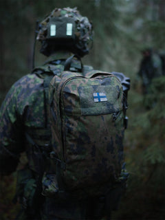 Person in camouflage uniform with a Savotta Niukka 20L backpack in a forest setting.