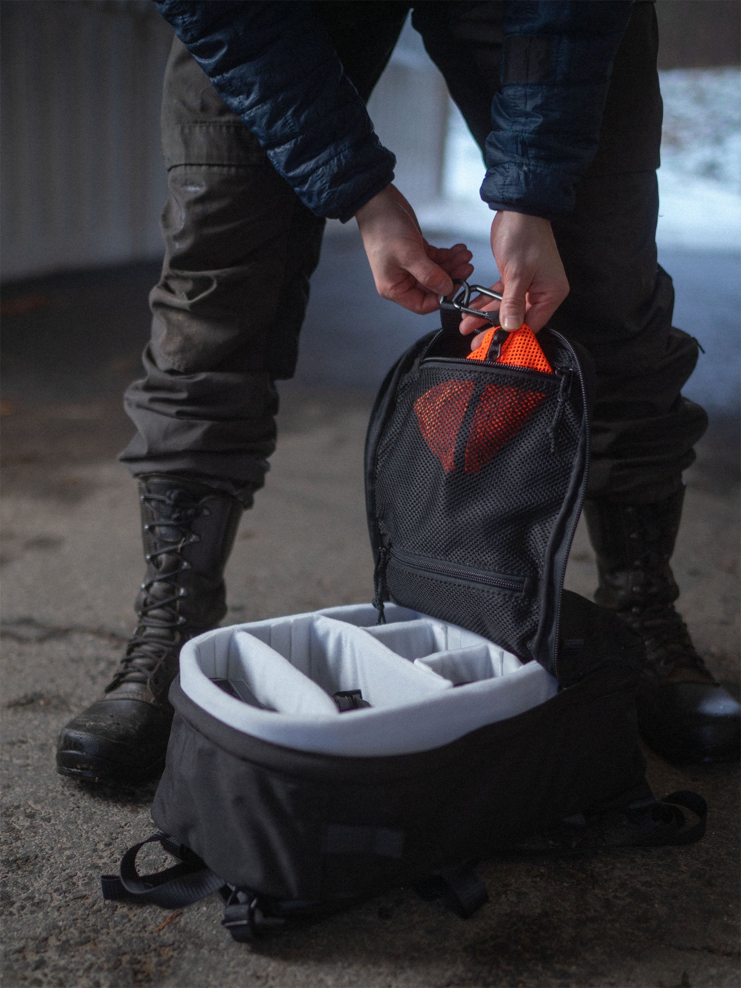 Person attaching a Savotta trinket pouch inside a black Savotta Niukka 20Lbackpack on a concrete floor.