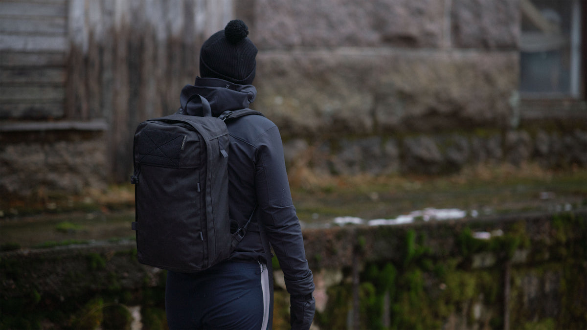 Sporty person with a Savotta Niukka 20L backpack walking away from the camera in an outdoor setting.