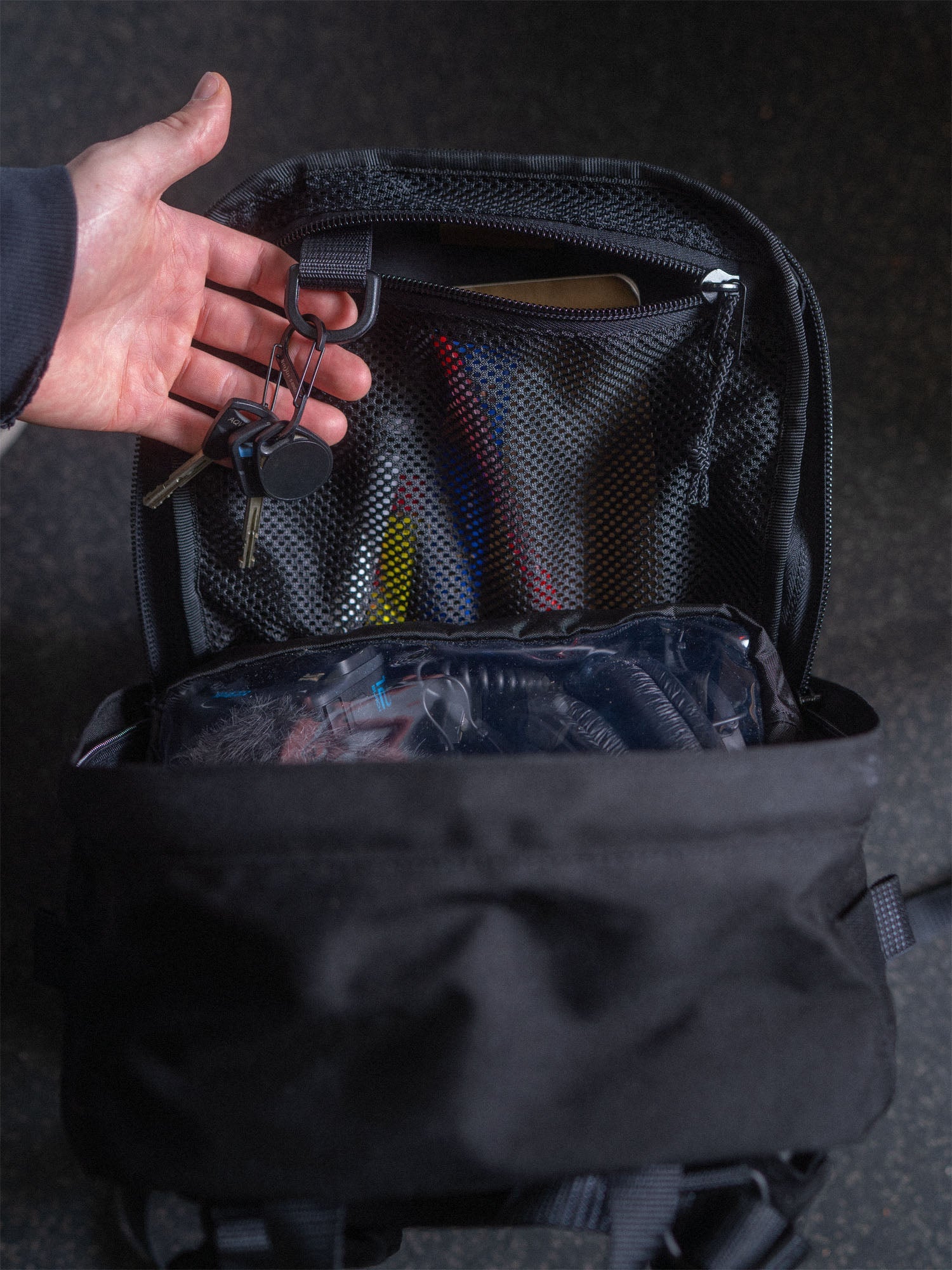 A black Savotta Niukka 20L backpack with items inside, hand showing the key holder inside the backpack