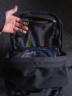 A black Savotta Niukka 20L backpack with items inside, hand showing the key holder inside the backpack