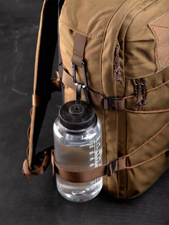 Brown Niukka 20L backpack with a Nalgene water bottle attached to the side with a carabine and the side compression strap on a dark background