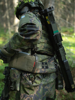 Person in camouflage military uniform inserting a Savotta S-IFAK insert into a Savotta S-IFAK horizontal mount which is attached to the Savotta plate carrier by dangler adapted in a forest setting