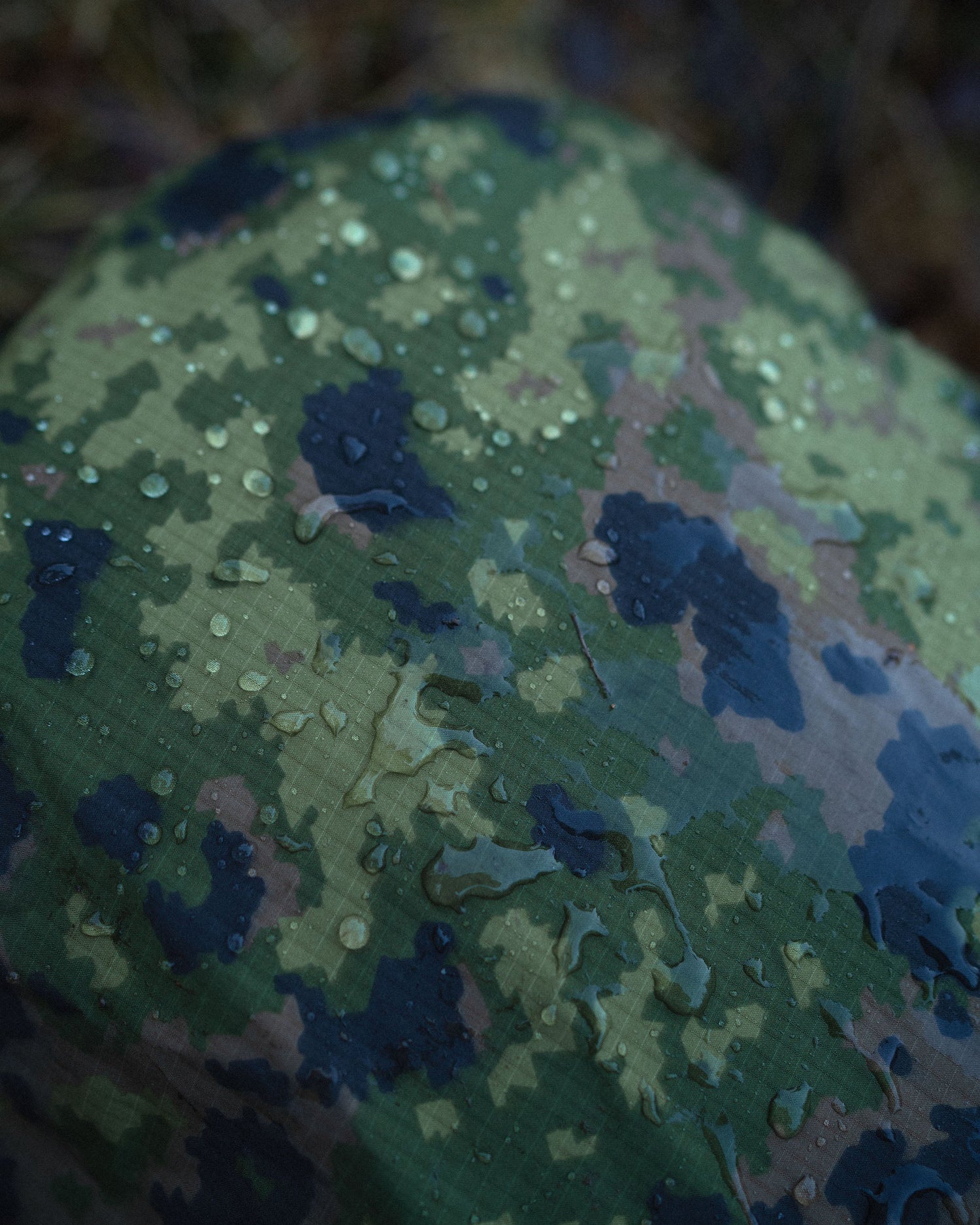 Close-up of a M05 camouflage-patterned Savotta 30L backpack cover with water droplets.