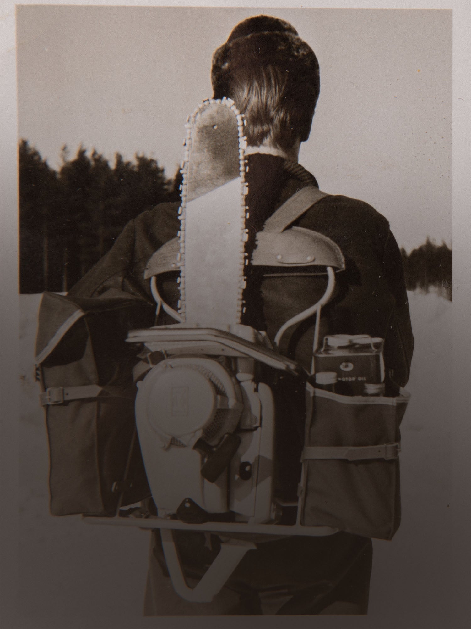 Old black and white photo of a person with a chainsaw attached to a Savotta backpack in a forest setting