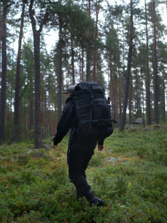 Person with a black Savotta Kantamus 60L backpack with a Savotta Askare hip pack attached walking through a forest