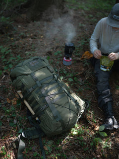 Person preparing food outdoors with a Savotta Kantamus 60L backpack next to them in the forest