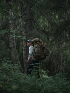 Person with a Savotta Kantamus 60L backpack with a Savotta Hatka 12L and side pouches 8L attached, walking through a forest
