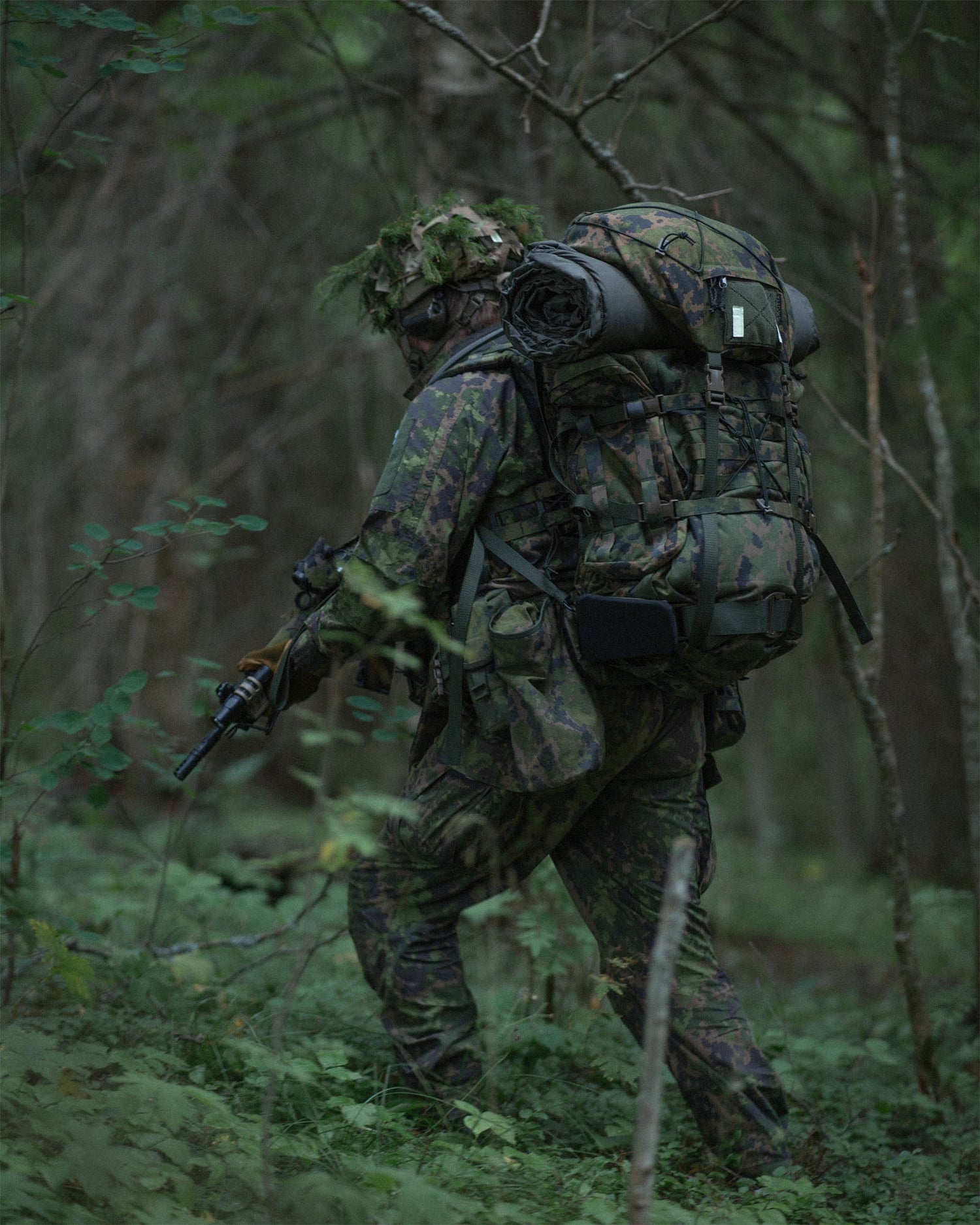 Person in camouflage gear with a Savotta Kantamus 60L backpack walking through a forest