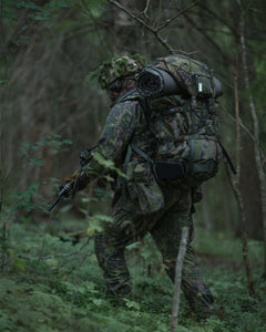 Person in camouflage gear with a Savotta Kantamus 60L backpack walking through a forest