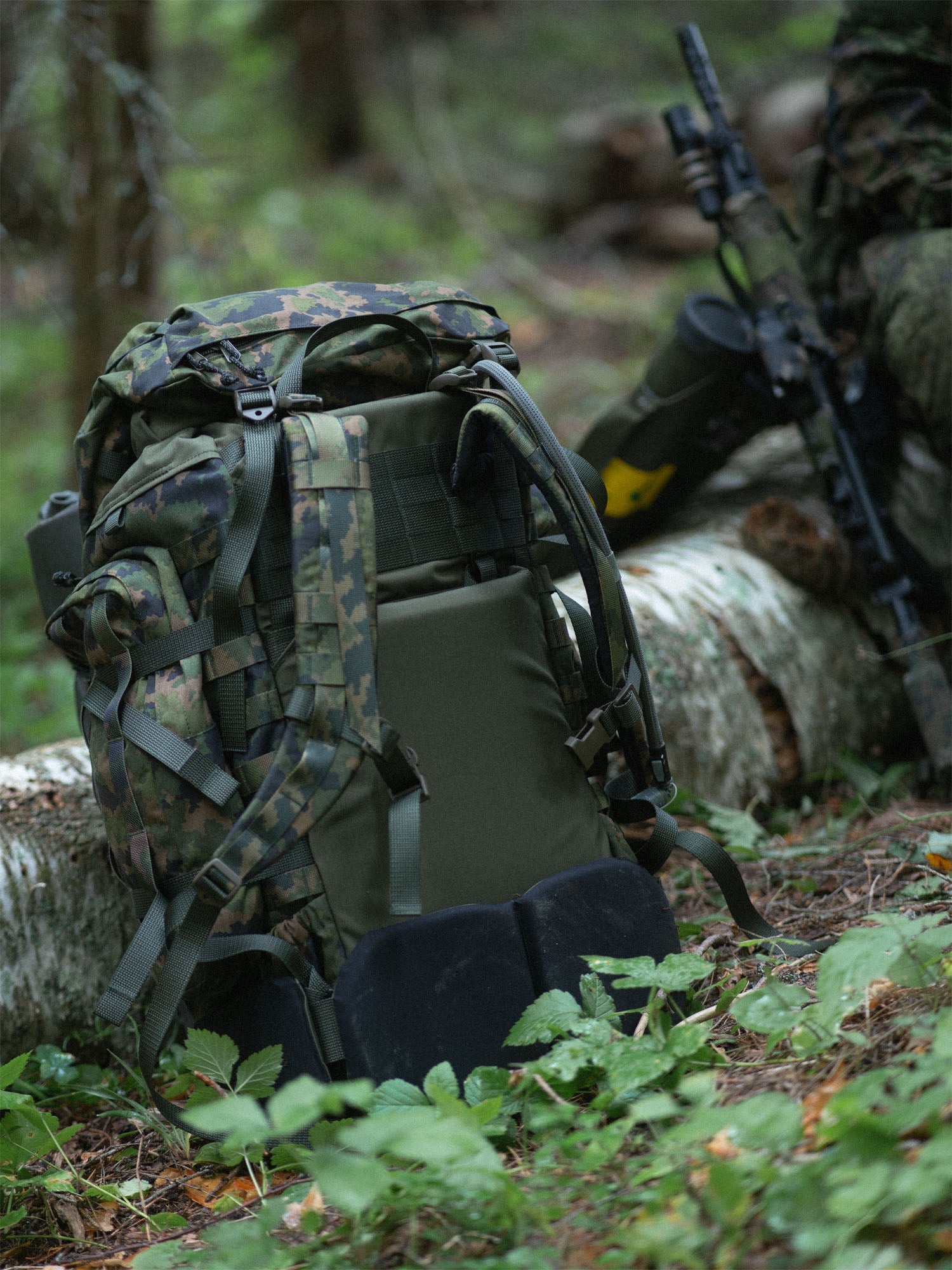Savotta Kantamus 60L backpack and rifle leaning against a log in a forest setting
