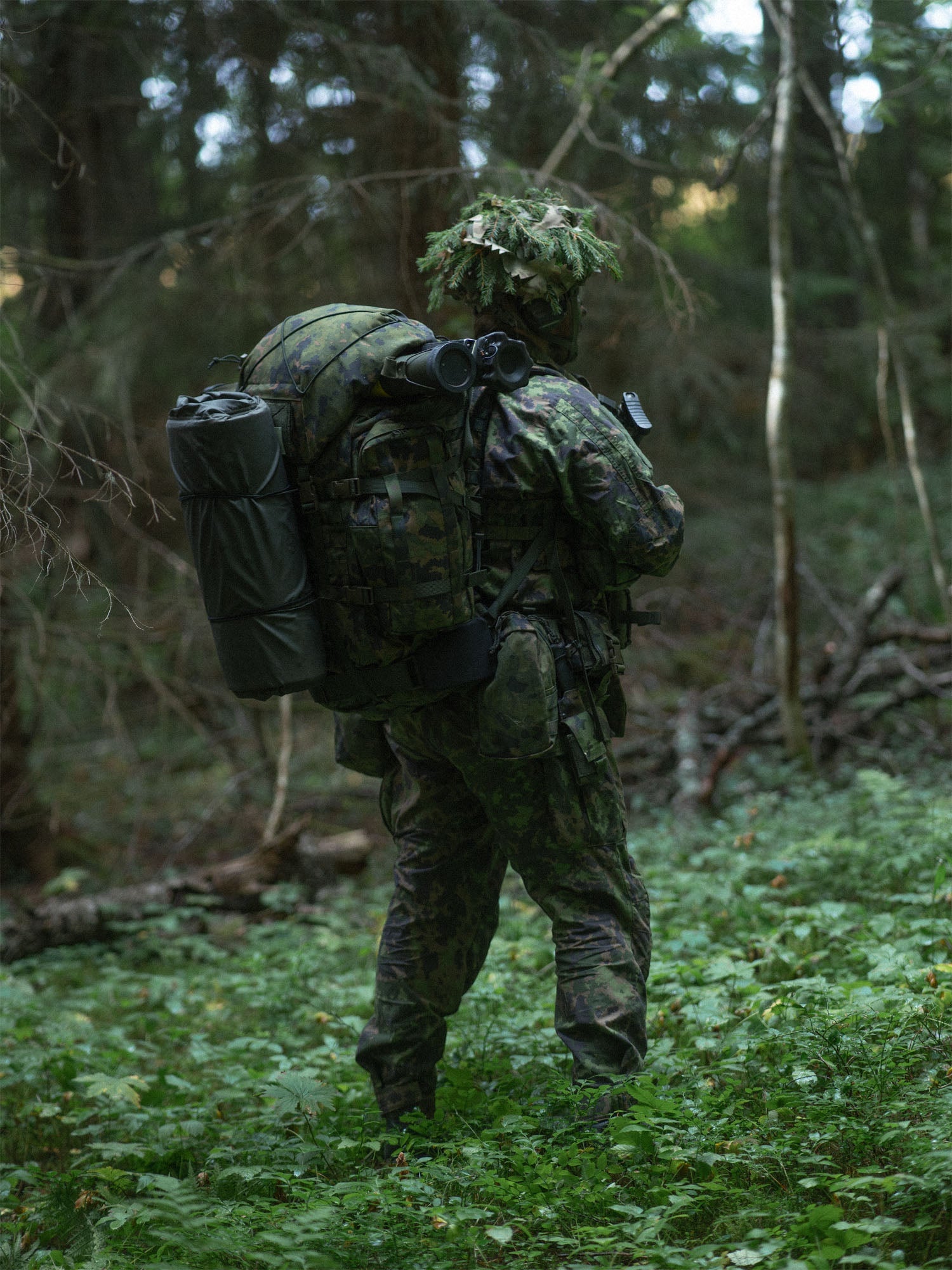 Person in camouflage gear with a Savotta Kantamus 60L backpack walking through a forest