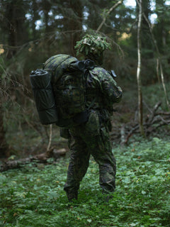 Person in camouflage gear with a Savotta Kantamus 60L backpack walking through a forest