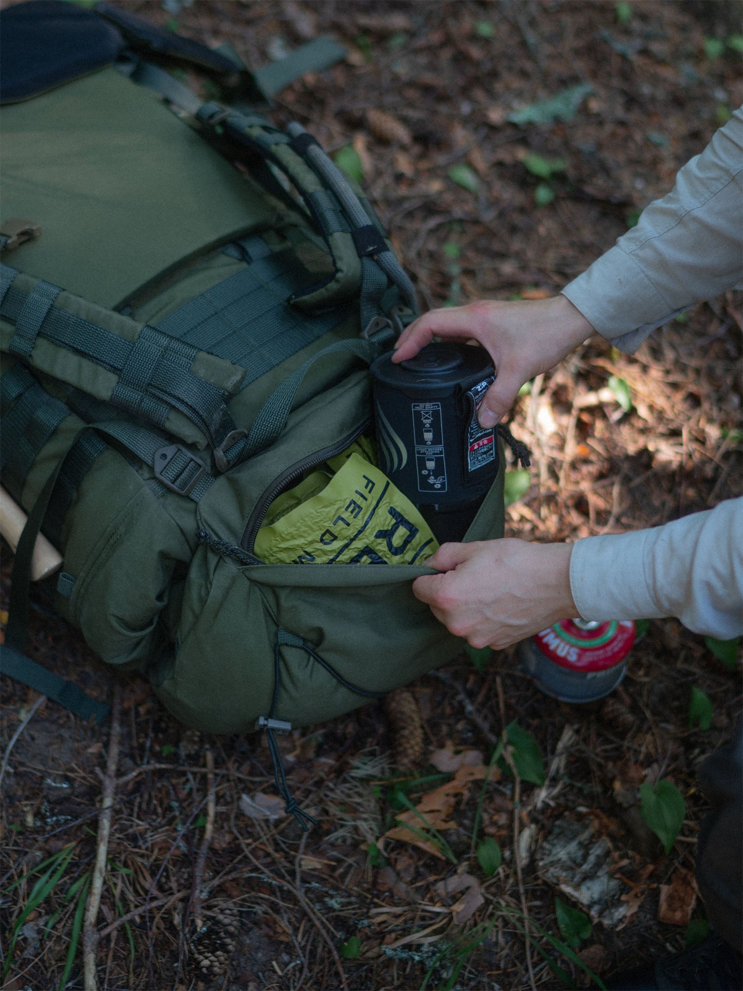 Person placing an item into the hat zipper pouch of a Savotta Kantamus 60L backpack outdoors.