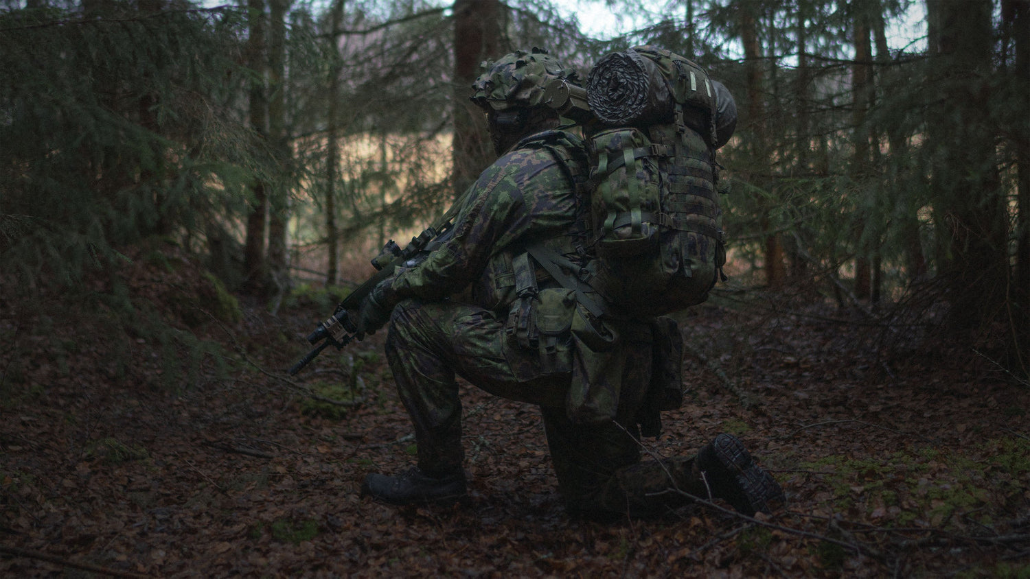 Person in camouflage gear with a Savotta Kantamus 40L backpack and rifle in a forest setting