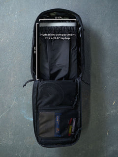 Opened black Savotta Niukka 20L backpack with the hydration compartment measurements (36×23 cm) showing how a 15.6" laptop fits inside, on a gray background