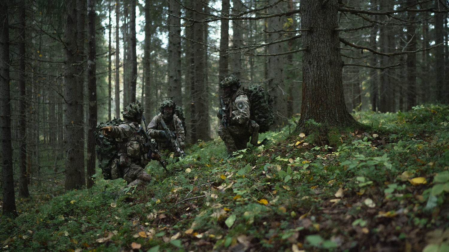 Three soldiers in camouflage gear moving through a forest.