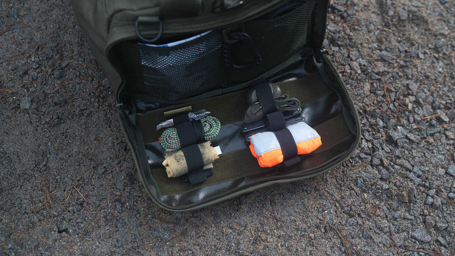 An opened Savotta bag showing the packing accessories on a gritty ground.