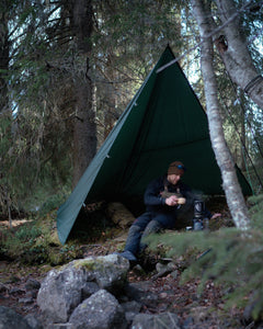 Person sitting inside a green Savotta Laavu tarp in a forest setting