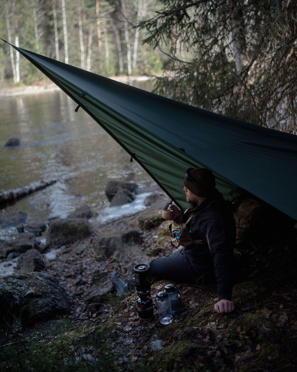 Person camping by a lake with a Savotta Laavu tarp as shelter
